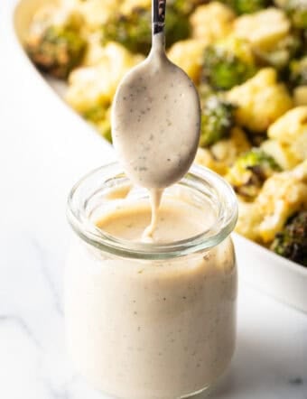 Spoonful of tahini sauce drizzling into a glass jar of dressing.