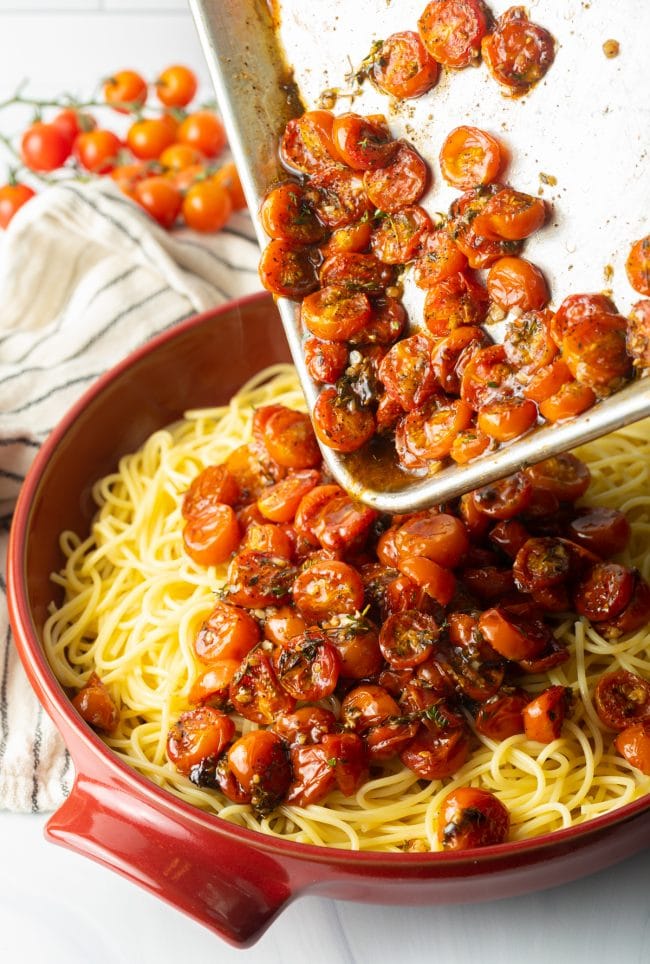 Pouring the roasted tomatoes from the baking sheet onto a bed of pasta. 