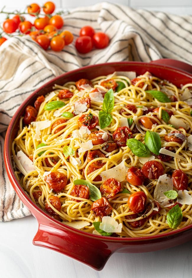 Side view of a bowl of roasted cherry tomato pasta sauce with spaghetti noodles. 