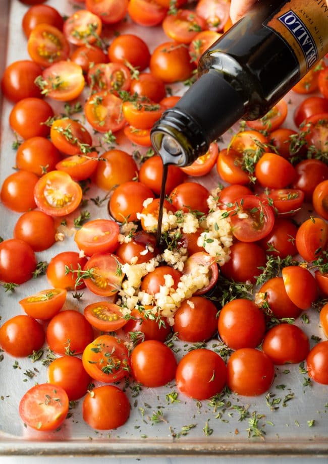 Pouring aged balsamic onto the pan of tomatoes with garlic and herbs.
