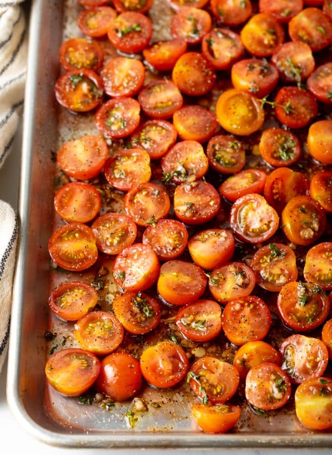 Coated tomatoes in vinegar, garlic, and herbs on a baking sheet before roasting. 