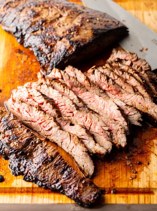 Seared steak sliced into thin strips on a wood cutting board.