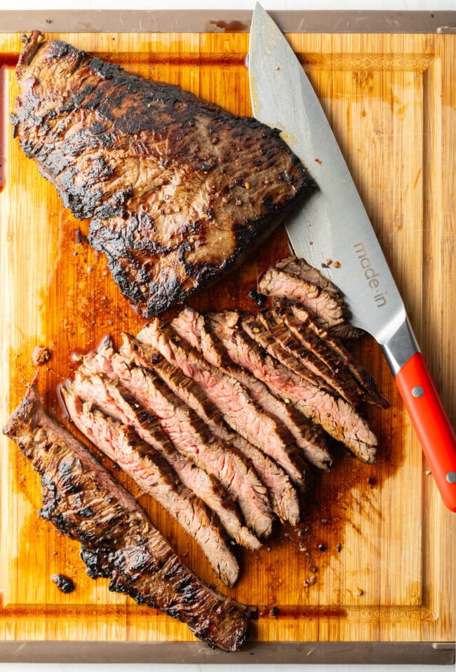 Seared steak sliced into thin strips on a wood cutting board, large knife to the side.