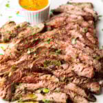 Thin slices of Bavette steak on a white serving platter with a ramekin of cowboy butter to the side.