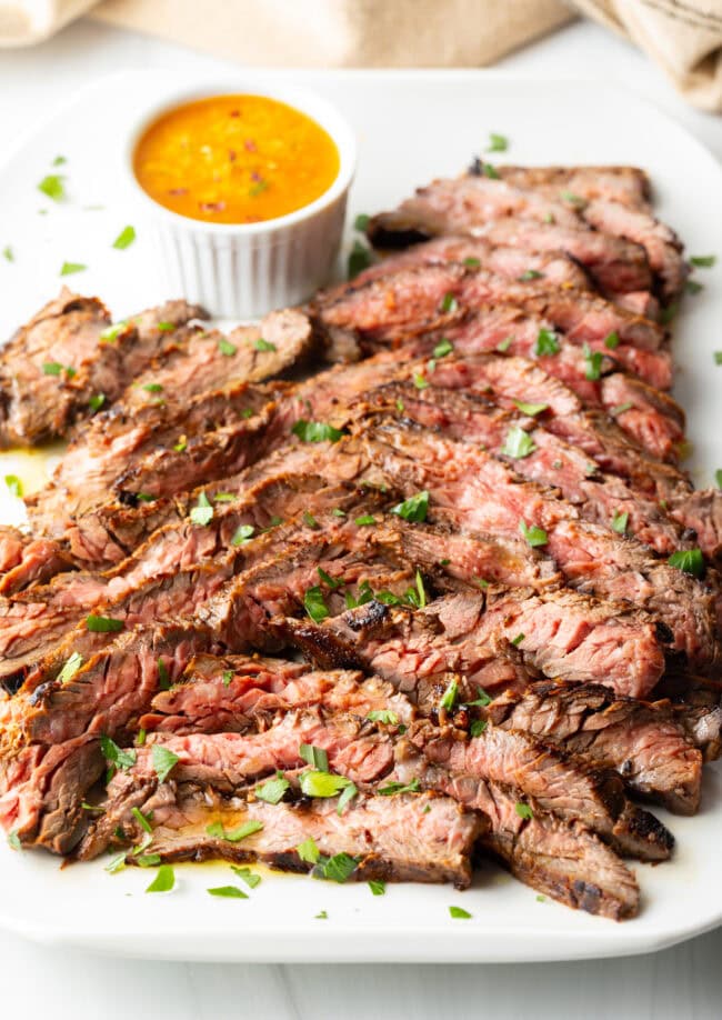 Thin slices of Bavette steak on a white serving platter with a ramekin of cowboy butter to the side.