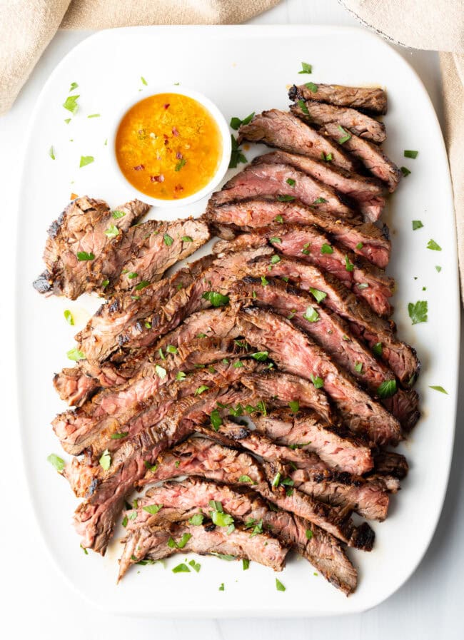 Thin slices of Bavette steak on a white serving platter with a ramekin of cowboy butter to the side.