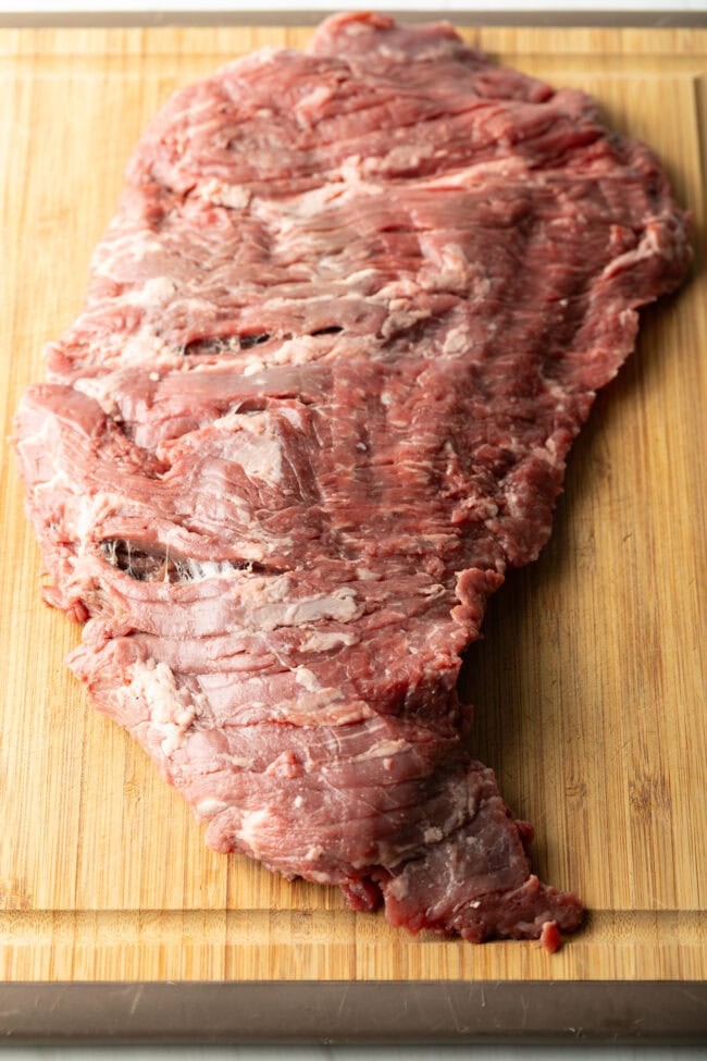 Large piece of raw beef on a wooden cutting board.
