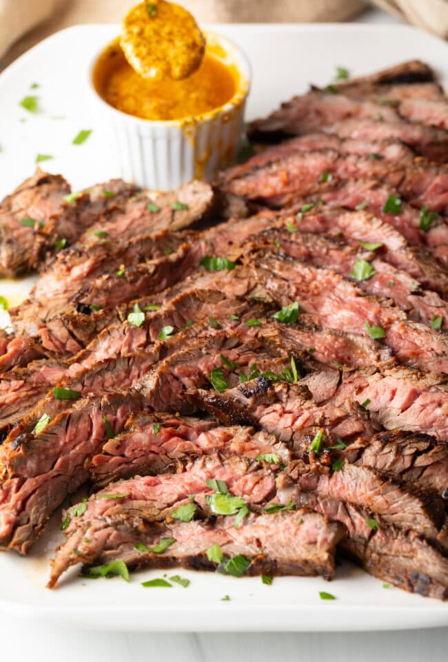 Thin slices of Bavette steak on a white serving platter with a ramekin of cowboy butter to the side.