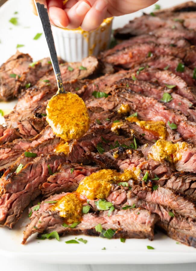 Hand spooning melted cowboy butter over thin slices of Bavette steak.