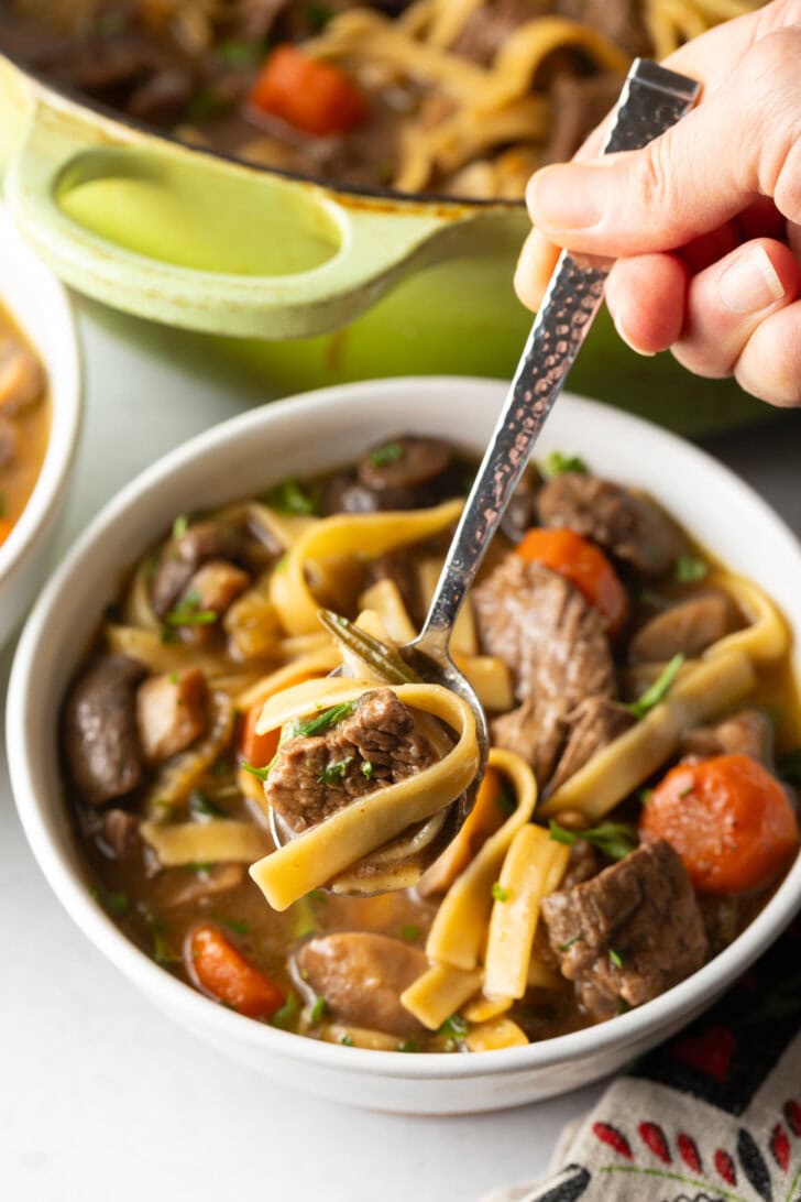 Bowl of beef noodle soup with a spoon holding a spoonful to camera.