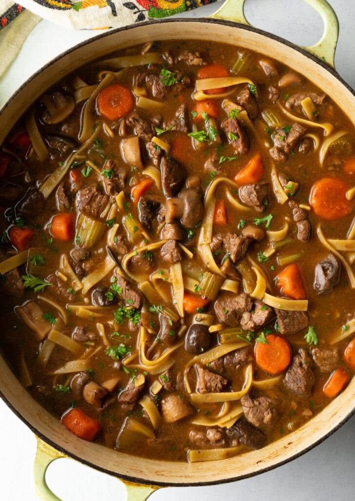 Top down view noodle soup with beef and veggies in a large pot.