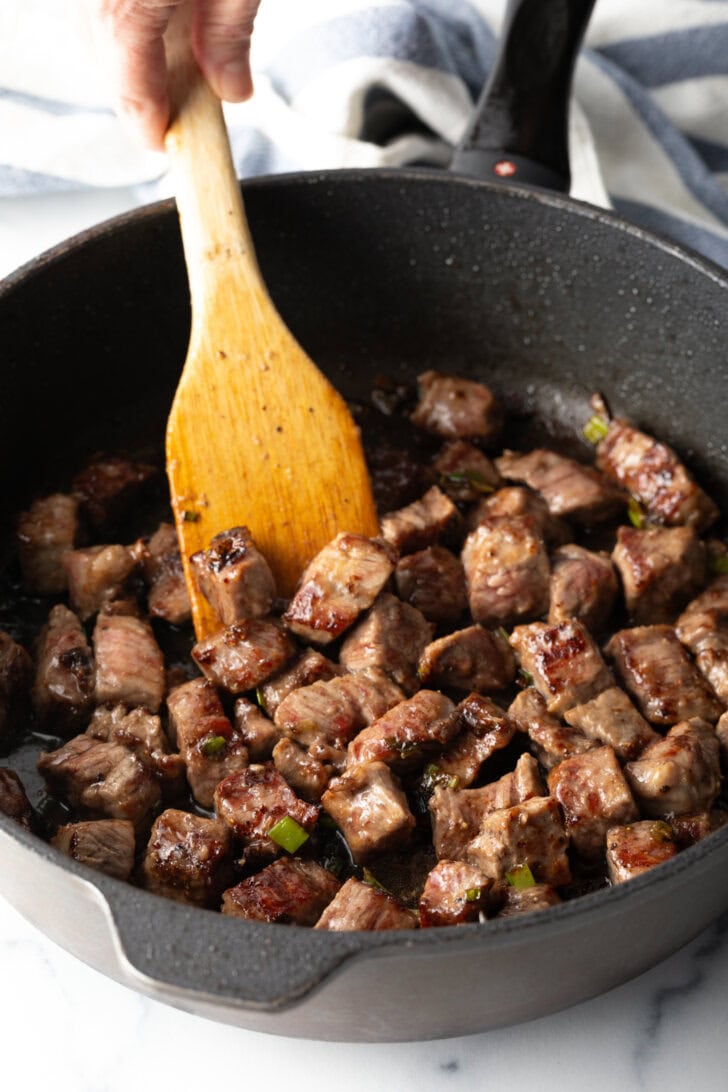 Wooden spoon stirring pieces of meat into a skillet with teriyaki sauce.