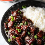 Bowl of beef teriyaki garnished with sliced green scallions, with white rice side-by-side in the bowl.