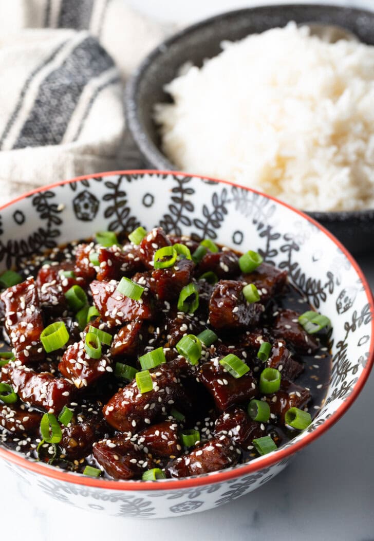Bowl of beef teriyaki garnished with sliced green scallions.
