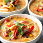 Three white and gray bowls filled with chicken taco soup. Each bowl is garnished with cilantro and red tortilla strips.