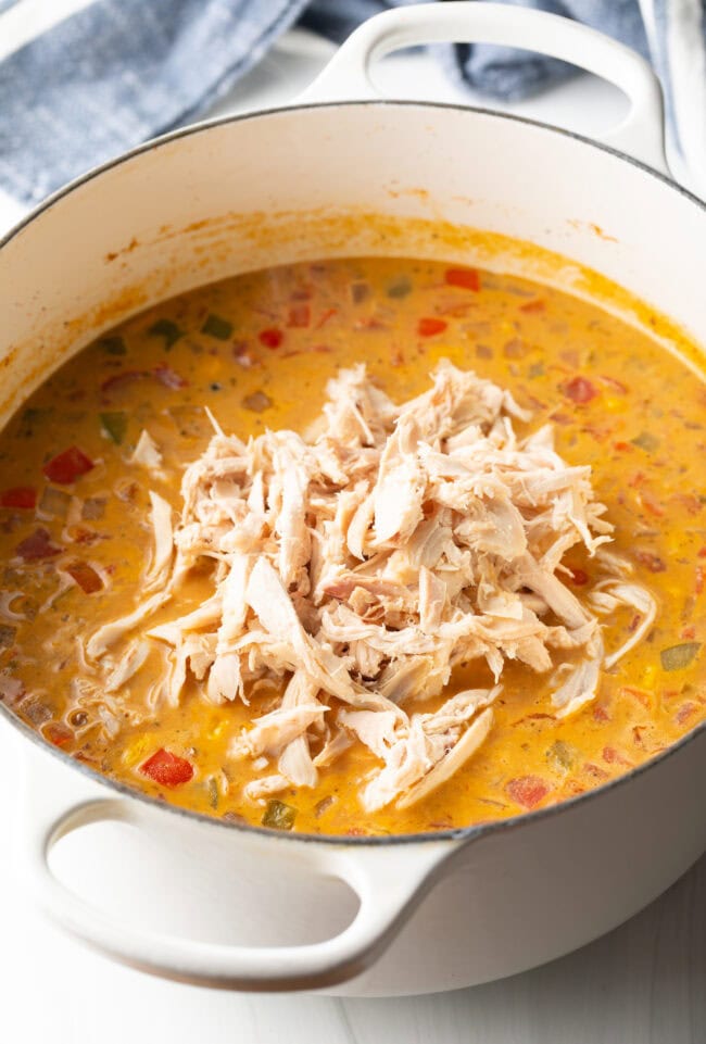 Creamy chicken, bean, and corn soup cooking in a white pot.