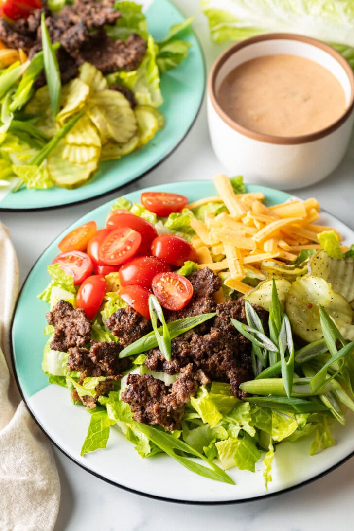 Loaded Big Mac cheeseburger salad with shredded lettuce, ground beef, halved grape tomatoes, shredded cheese, pickles, and sliced green onion.