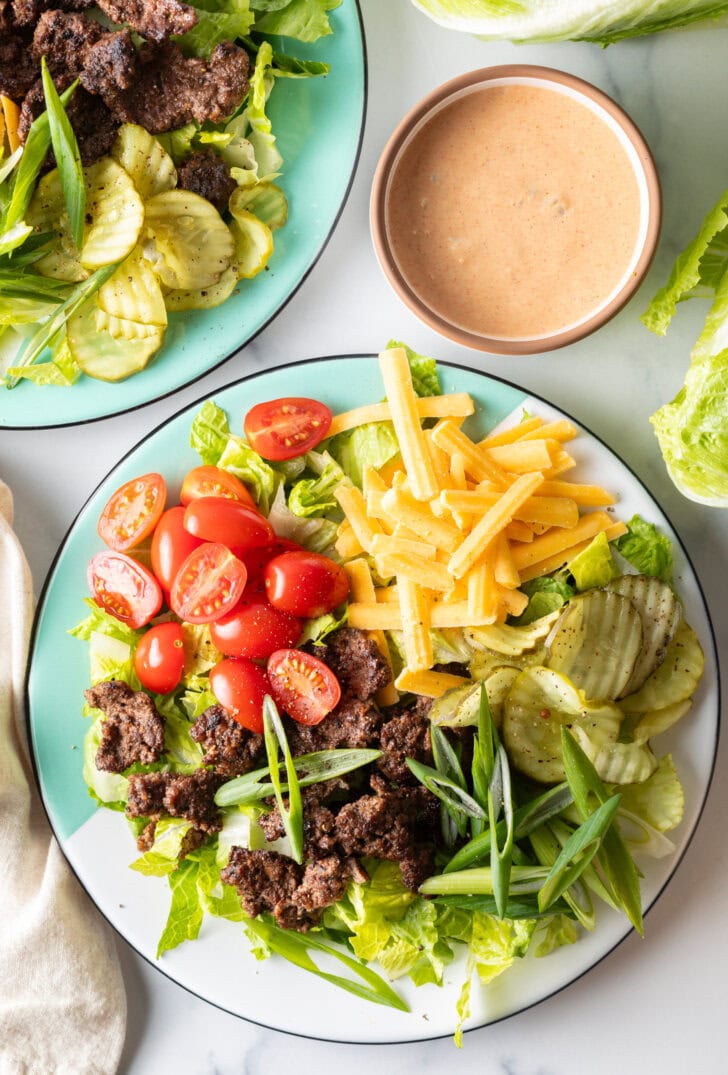 Loaded Big Mac cheeseburger salad with shredded lettuce, ground beef, halved grape tomatoes, shredded cheese, pickles, and sliced green onion.