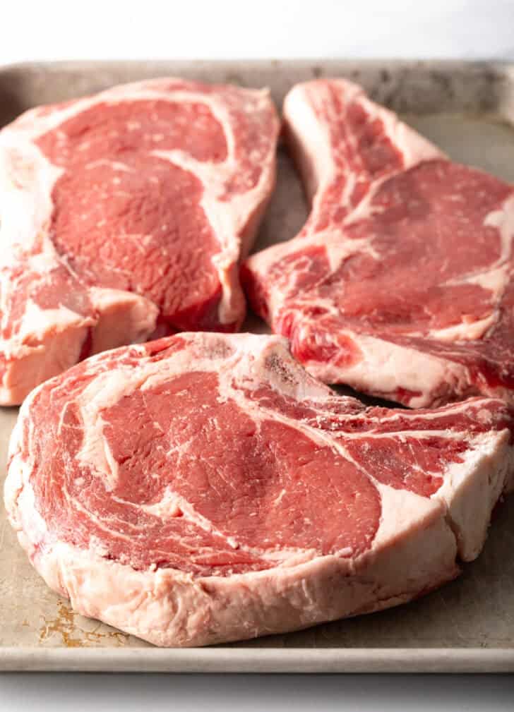 3 raw bone in steaks with fat marbling.