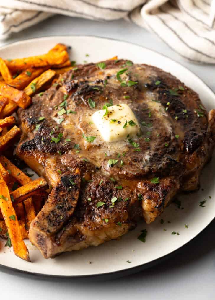 Large bone in ribeye steak on a plate with sweet potato fries.