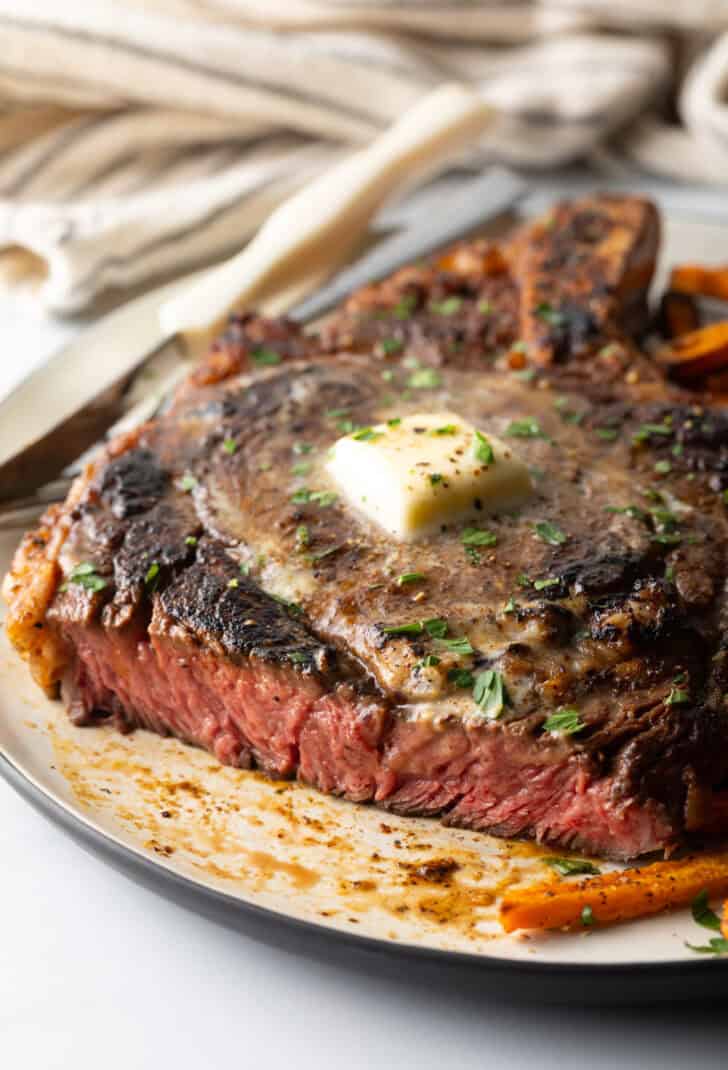 Large bone-in ribeye steak on a plate with sweet potato fries. The steak has been sliced to show the medium rare meat inside.