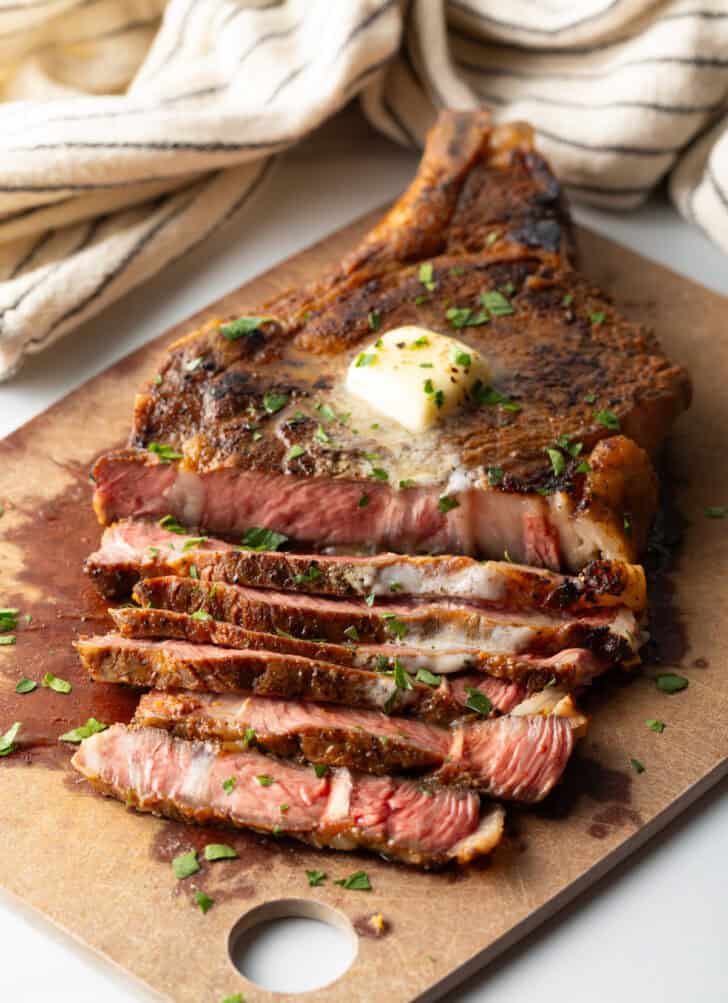 Ribeye steak on a cutting board. Half of the meat has been cut into slices, showing the medium rare inside.