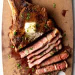 Ribeye steak on a cutting board. Half of the meat has been cut into slices, showing the medium rare inside.