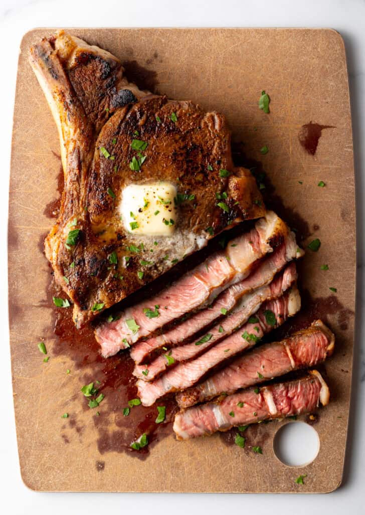 Ribeye steak on a cutting board. Half of the meat has been cut into slices, showing the medium rare inside.