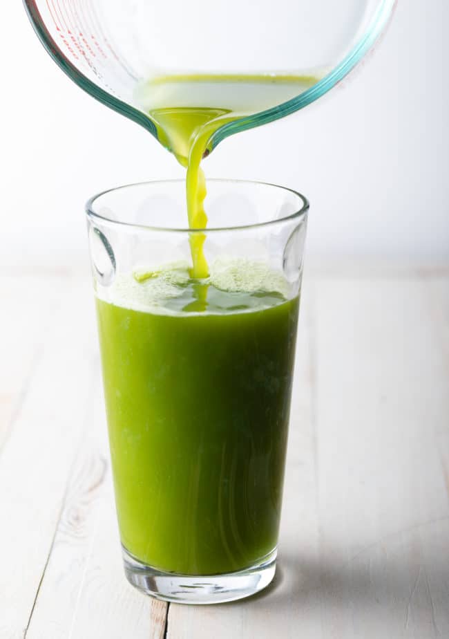Pouring celery juice from a pitcher into a glass. 