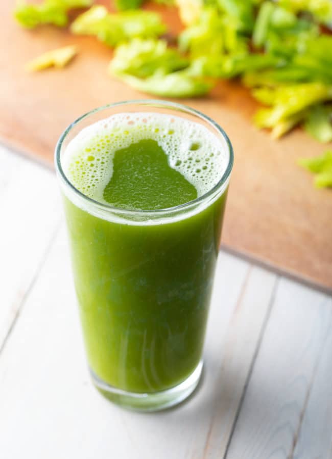 Large glass of celery juice with celery on a cutting board in the background.