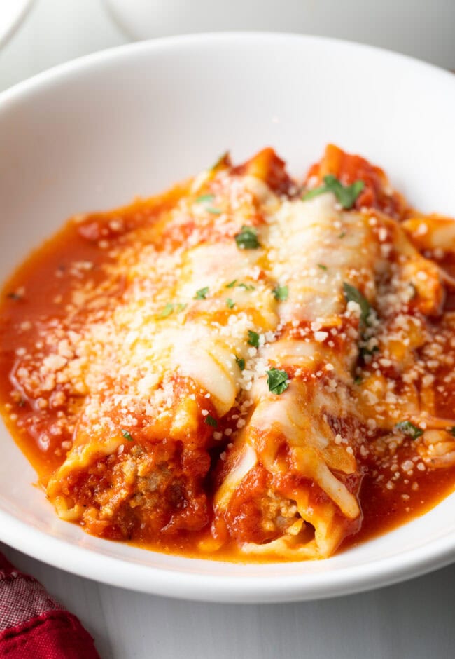 Two pieces of cheese manicotti with meat in a white pasta bowl.