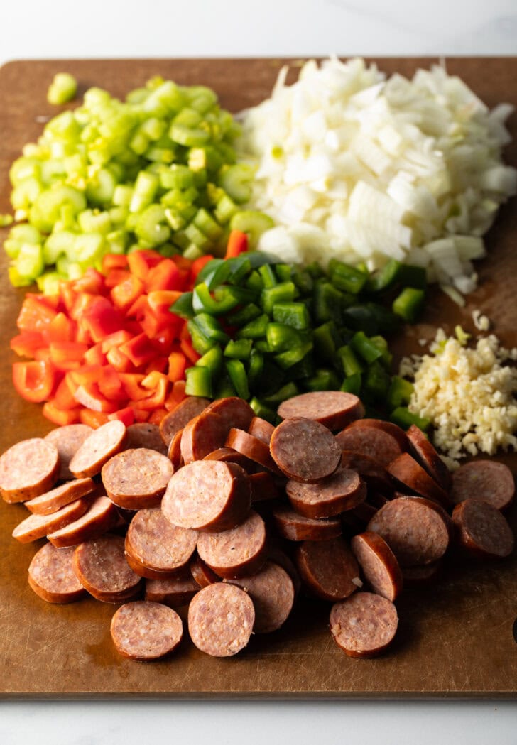 Chopped recipe ingredients on a cutting board: Sausage, red peppers, green peppers, garlic, onion, and celery.