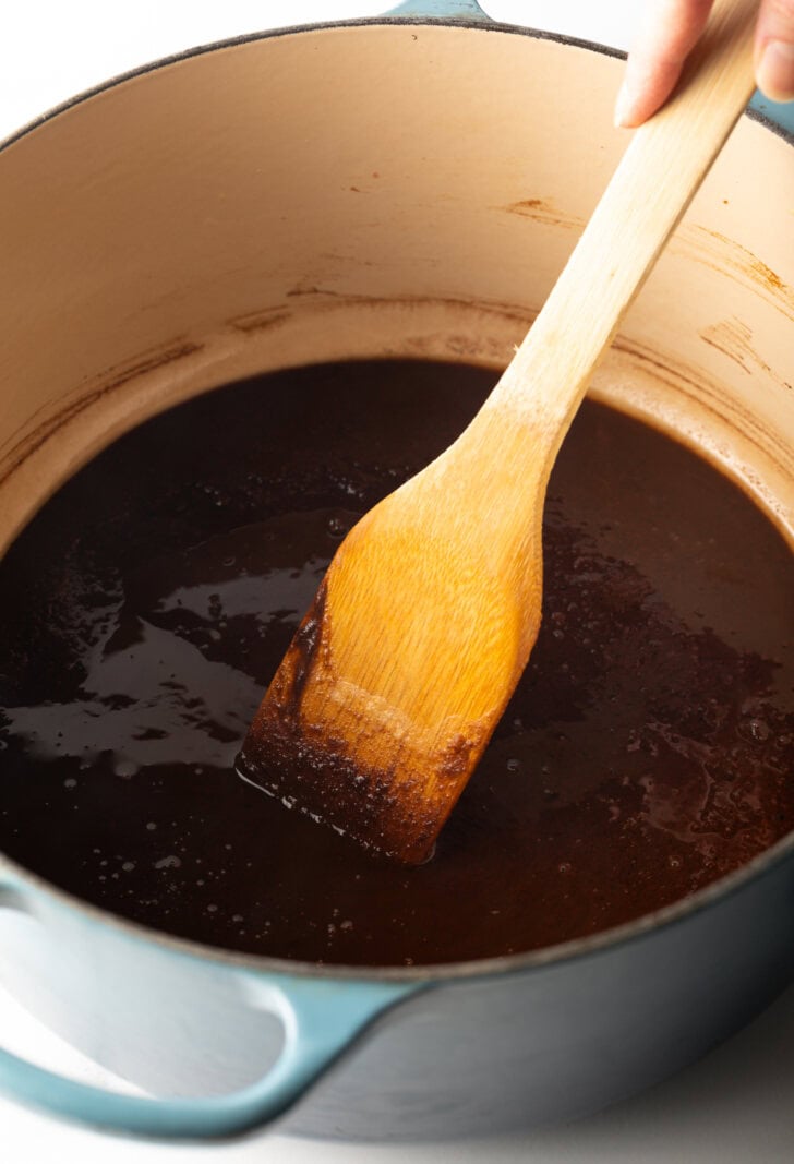 Wood spatula stirring dark brown roux in a cooking pot.