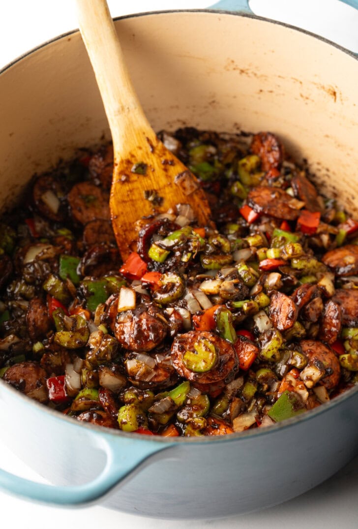 Chopped peppers, onion, and celery in a cooking pot, being stirred by a wooden spatula.