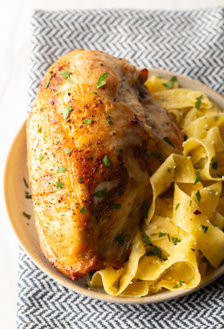 Bourbon brined chicken breast on a white plate with side of buttery noodles.