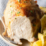Bourbon brined chicken breast on a white plate with side of buttery noodles. A large bite has been removed from the chicken to show the moist interior.