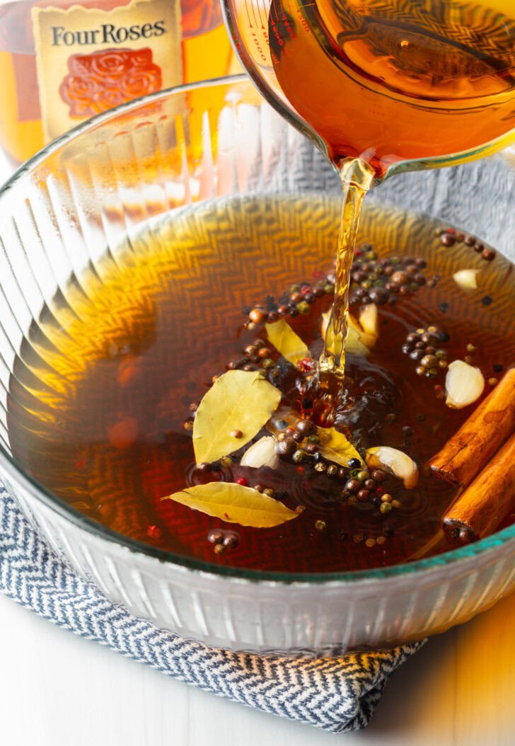 Adding bourbon to the brine in a glass bowl.