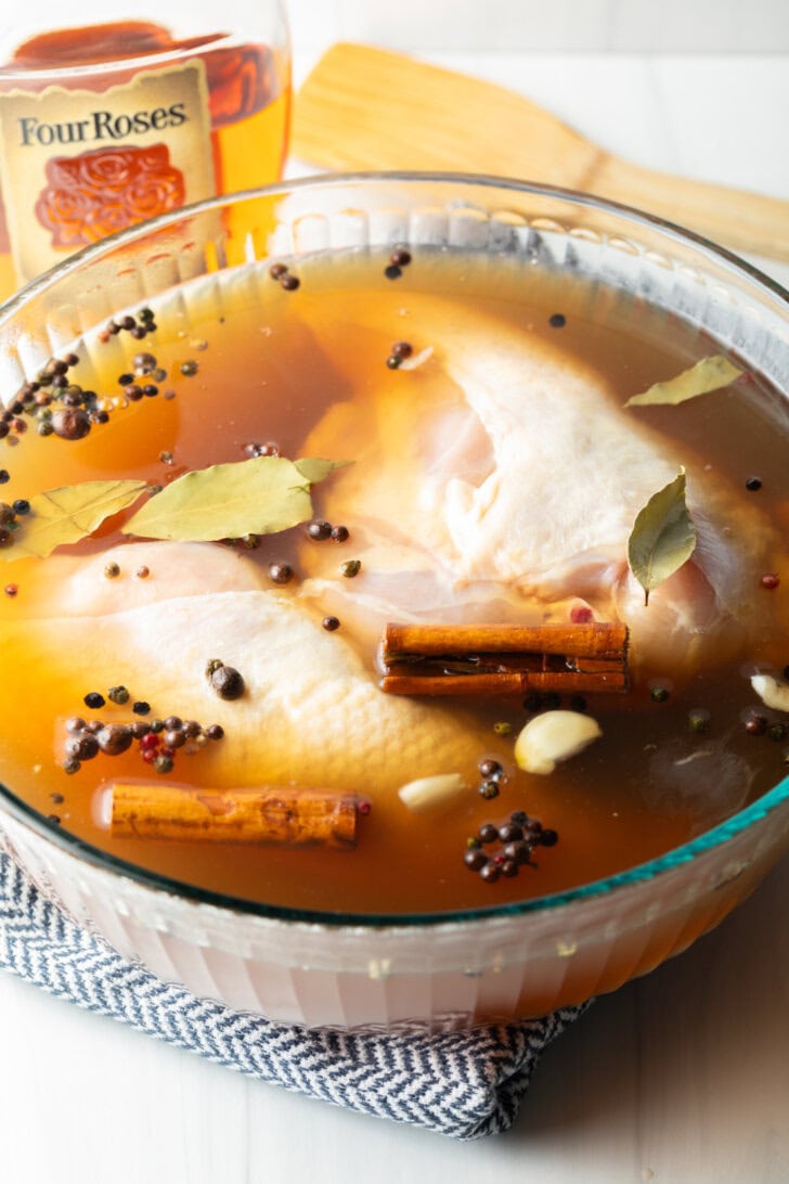 Two chicken breasts soaking in a clear bowl with bourbon brine.
