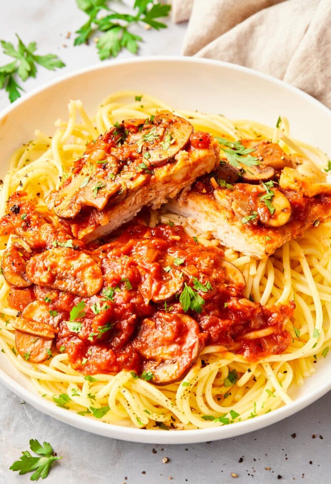 Chicken with tomato sauce and spaghetti noodles on a white plate, cut into pieces