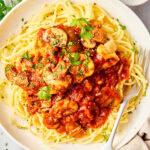 Chicken with tomato sauce and spaghetti noodles on a white plate.