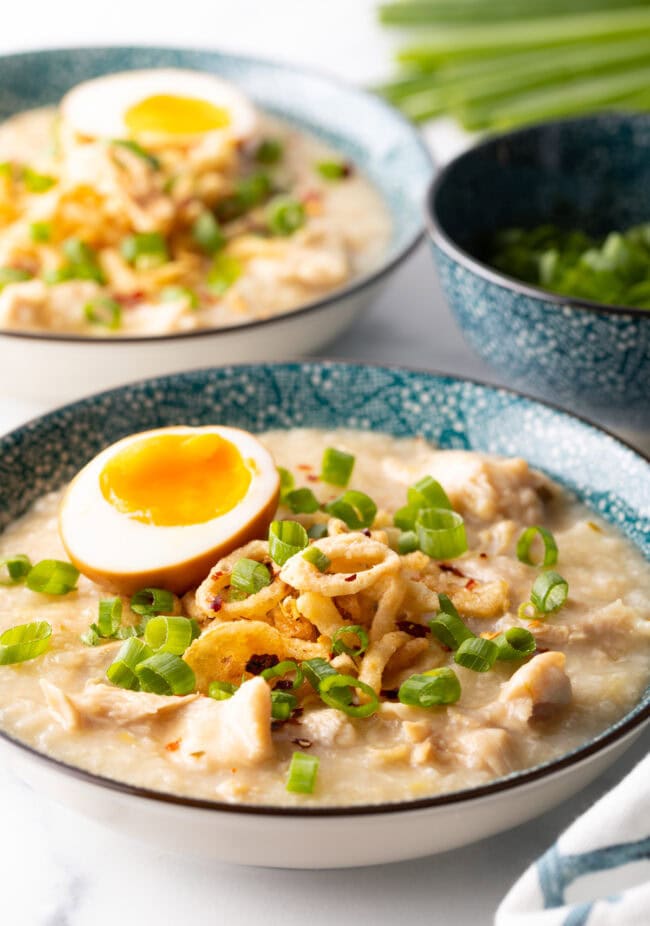 Finished bowl from chicken congee rice porridge recipe, loaded with fried onions, scallions, and soft boiled egg.