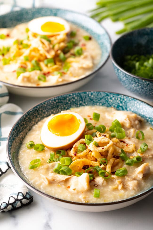 Bowl of rice porridge loaded with chopped scallions, fried onion, and soft boiled egg.