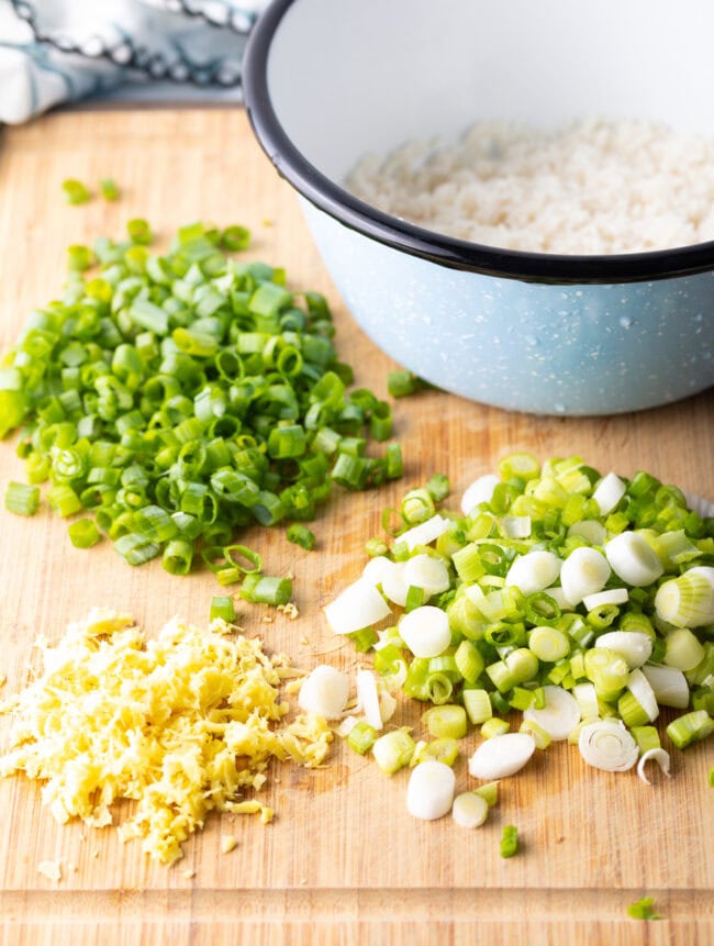 Fresh grated ginger, chopped white, and chopped green scallions on a wood cutting board.