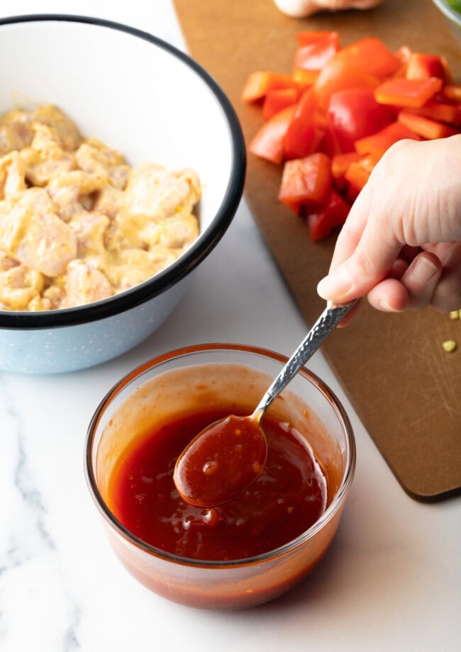 Hand stirring red sauce in a small glass dish.