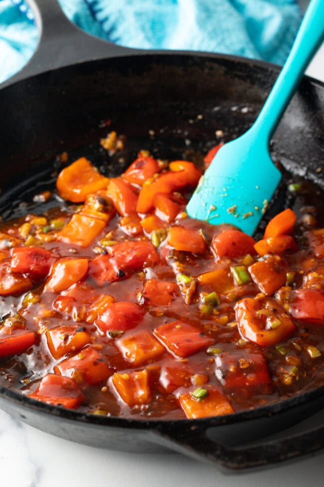 Blue spatula stirring chicken pieces and red peppers in a skillet.
