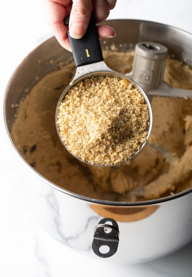 adding measuring cup of ground walnuts to the standing mixer bowl