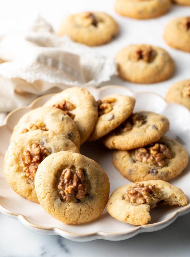 plate of 8 chocolate chip walnut cookies on a plate, one cookie with bite taken