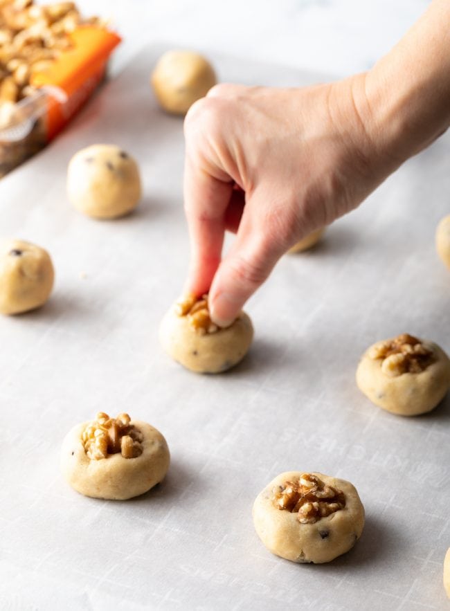 hand adding walnut half to each raw cookie dough ball