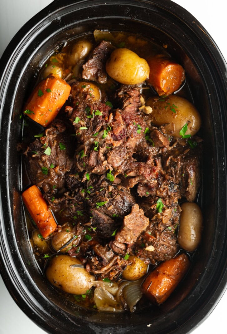 Pot roast cooked in a crock pot, with baby potatoes and large carrot chunks.