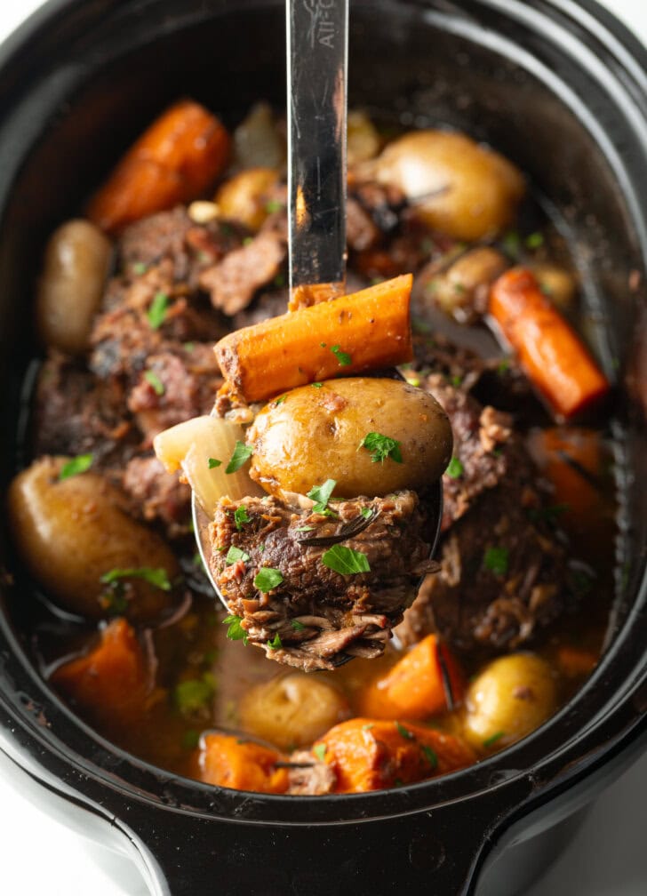 Large metal spoon with serving of slow cooker pot roast held to camera.